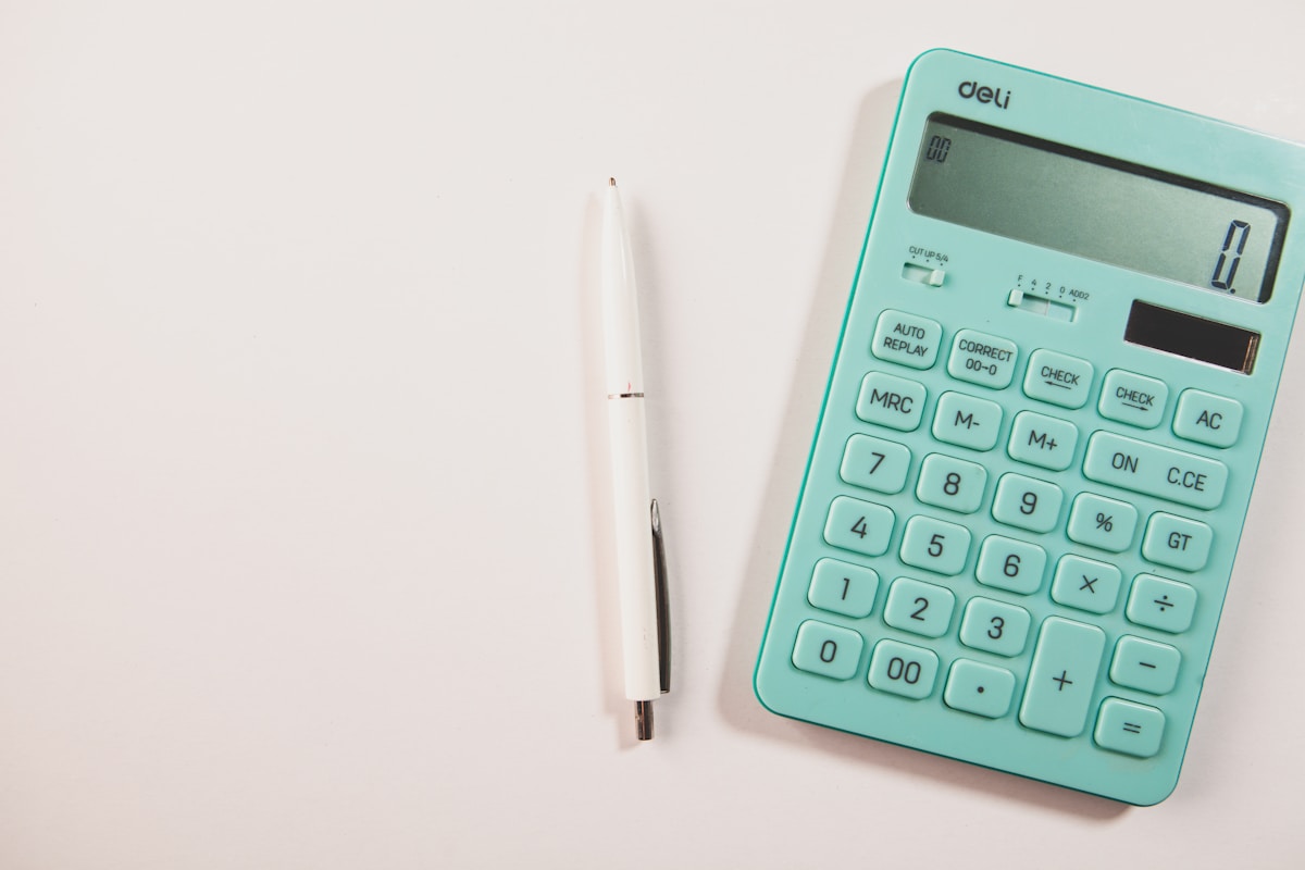 Calculatrice de bureau turquoise et stylo blanc sur fond blanc.
