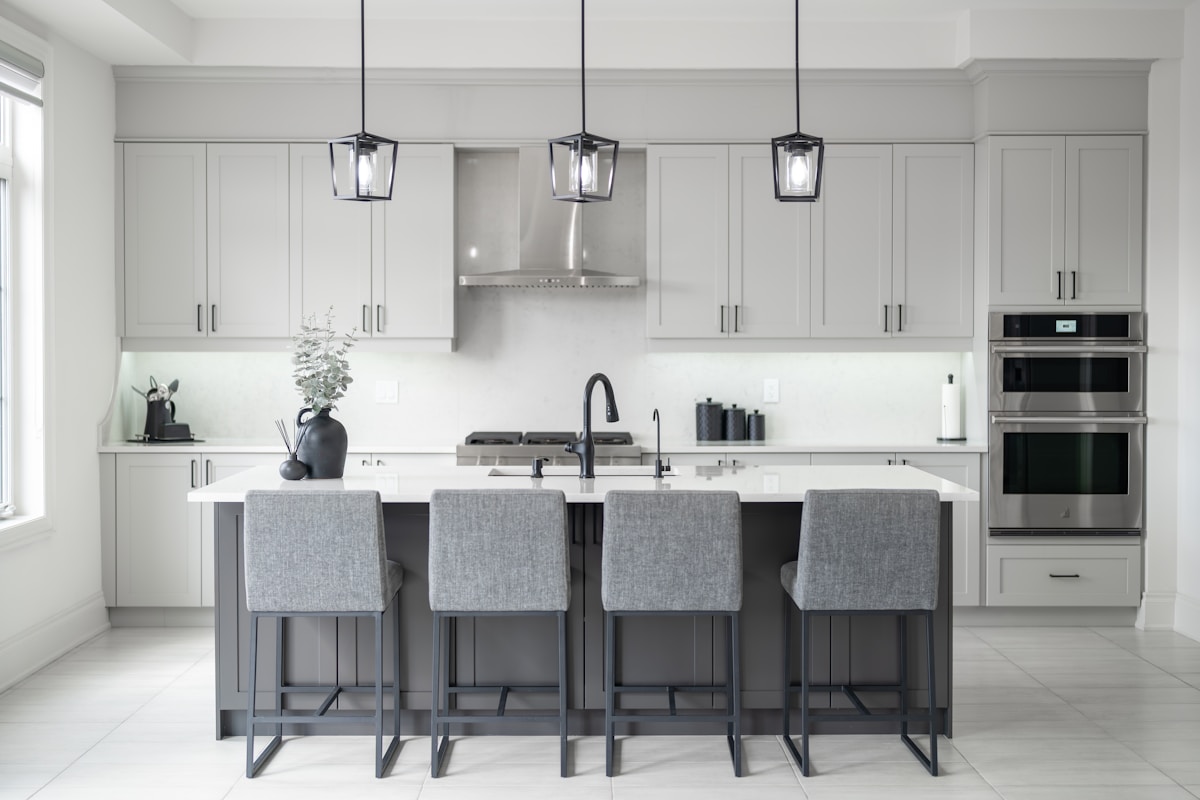 Cuisine moderne et élégante avec armoires grises, îlot central et luminaires suspendus.