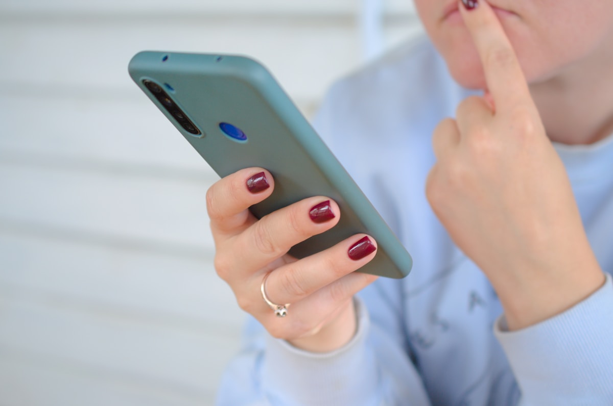 Mains tenant un téléphone portable vert avec des ongles vernis en rouge.