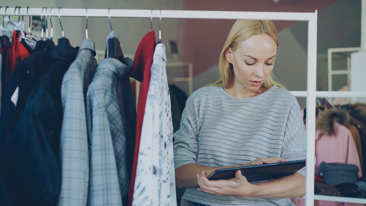 Femme blonde examinant des vêtements sur un portant dans un magasin.