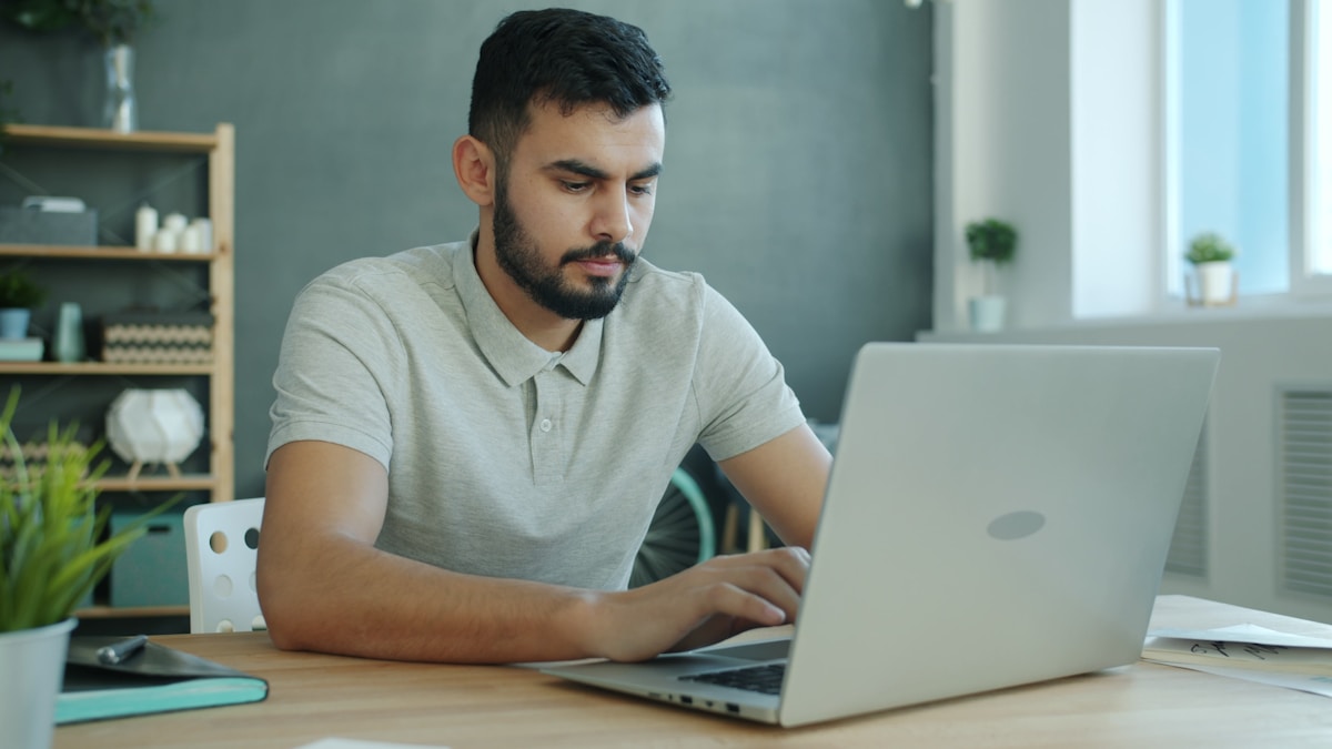 Homme barbu concentré travaillant sur ordinateur portable dans un bureau.