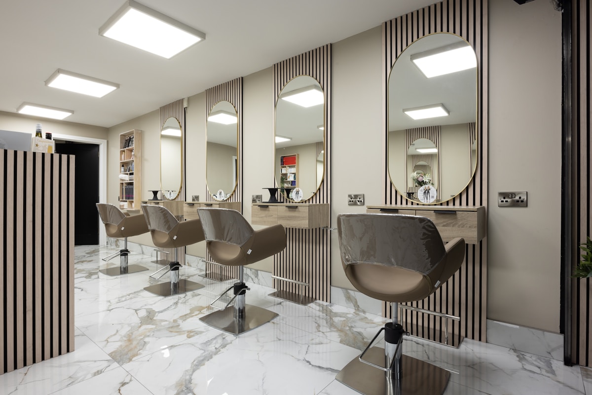 Salon de coiffure moderne avec miroirs, chaises et sol en marbre.