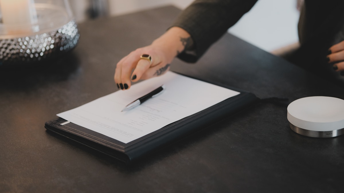 Personne écrivant sur un formulaire avec un stylo sur un bureau.
