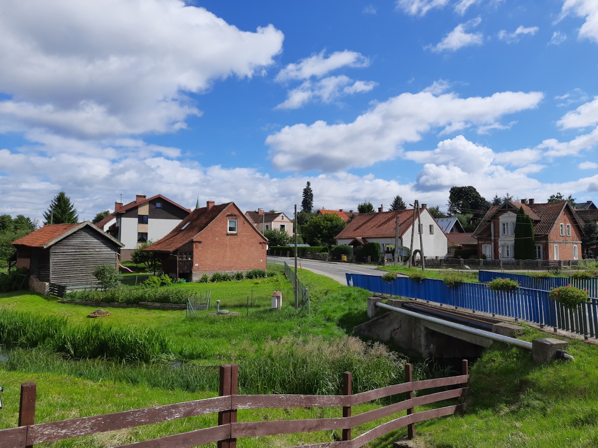 Village rural avec maisons traditionnelles, prairies verdoyantes et pont sur un cours d'eau.