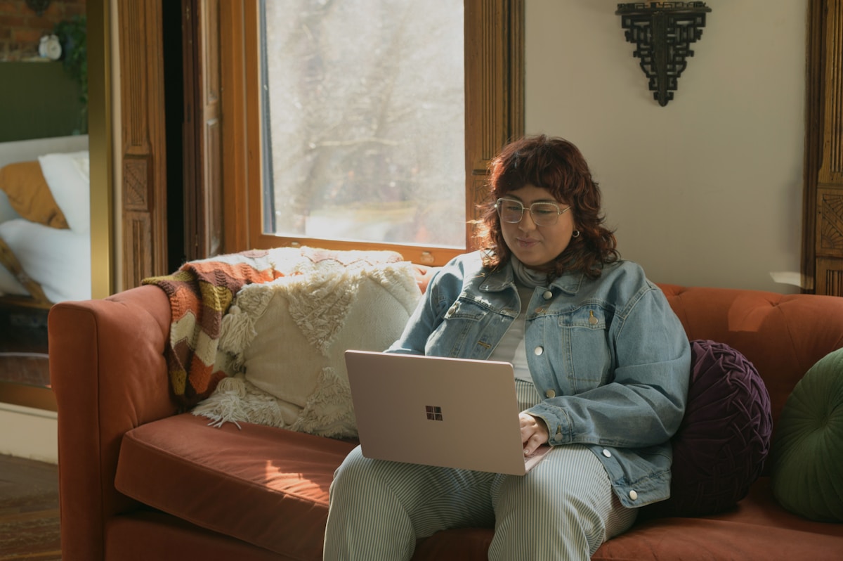 Femme assise sur un canapé, utilisant un ordinateur portable dans un intérieur confortable.