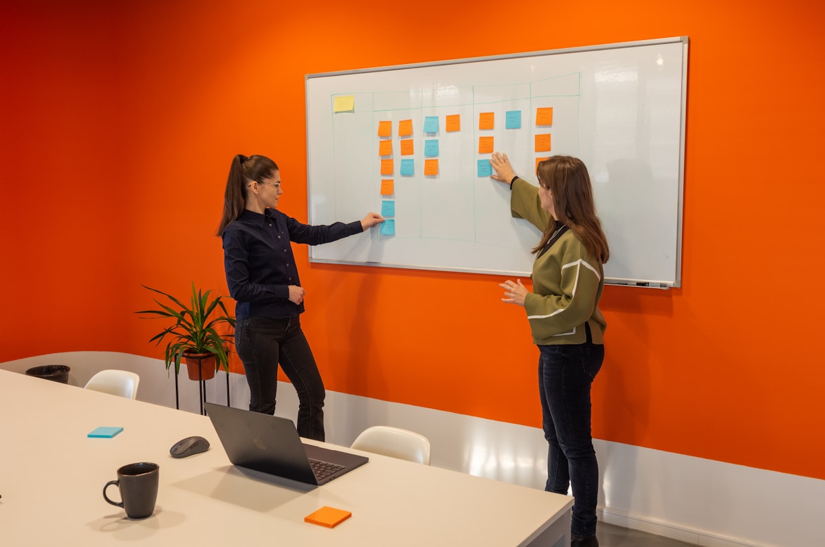 Deux femmes travaillant ensemble sur un tableau blanc dans un bureau coloré.