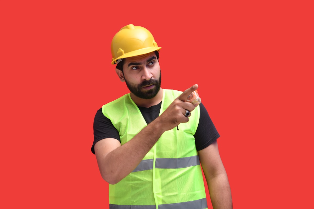 Homme en gilet de sécurité jaune et casque de chantier pointant du doigt.