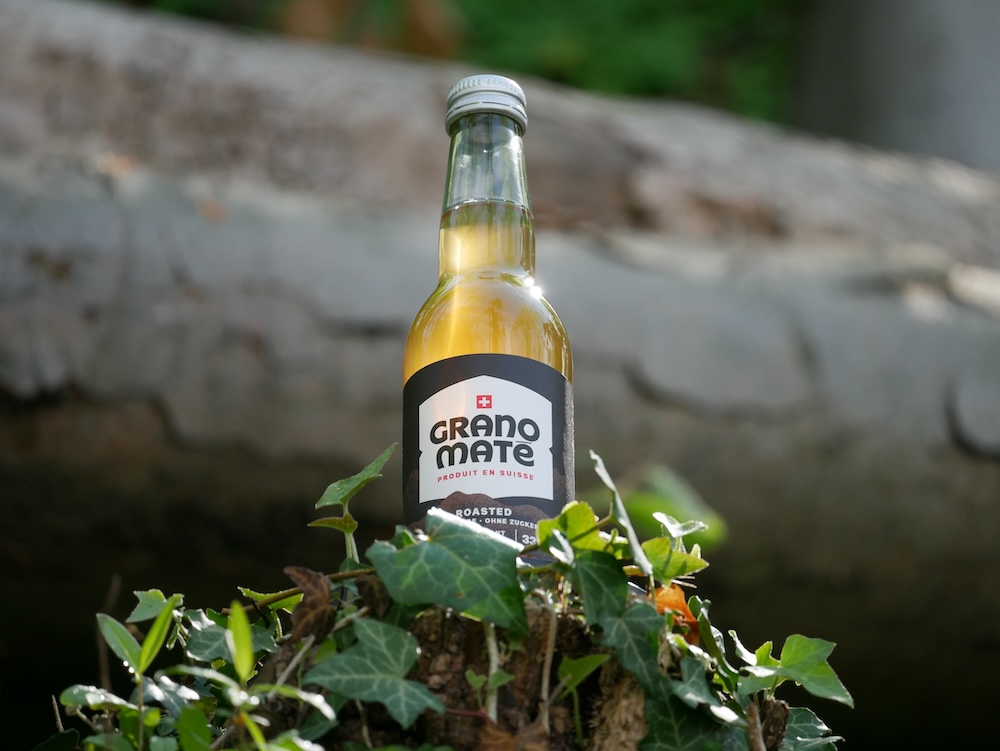 Une bouteille de Grano Maté dans une forêt suisse, symbolisant son origine locale.