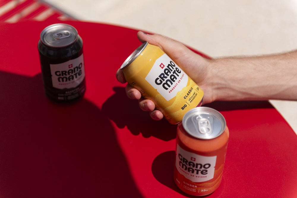 Trois canettes de Grano Maté BIO sur une table rouge d'extérieur d'un commerce