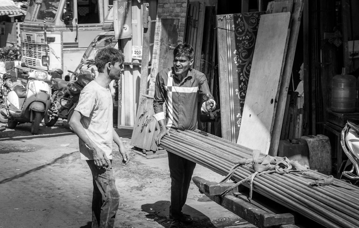 Two men carrying lumber in a market.