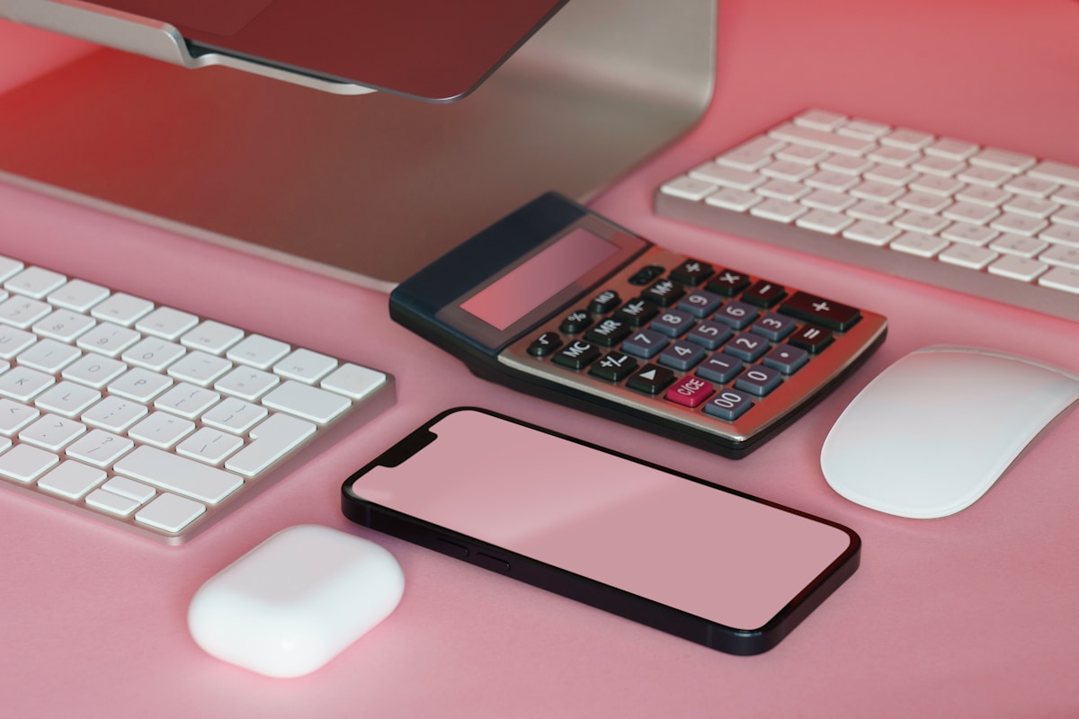 Ordinateur portable, clavier, souris, calculatrice et téléphone portable sur fond rose.