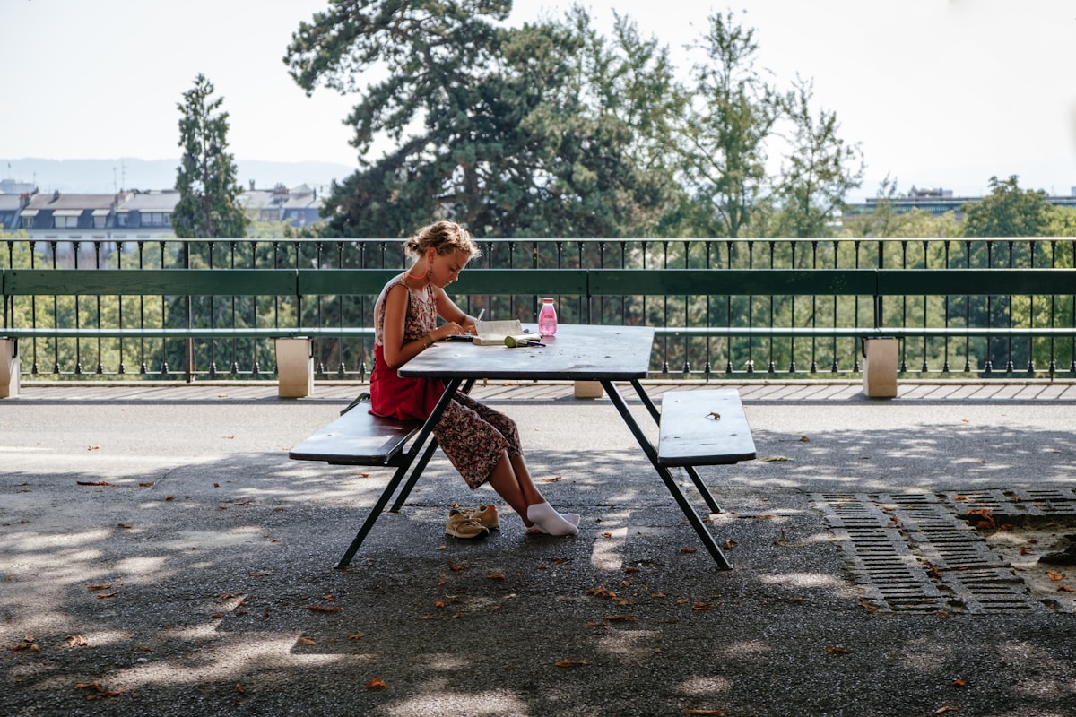 Jeune femme assise à une table extérieure, dessinant ou écrivant.