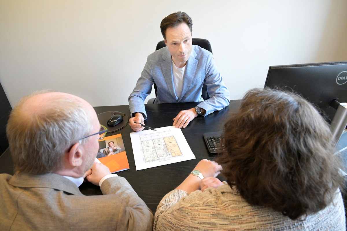 Trois personnes discutent autour d'un plan architectural sur un bureau.