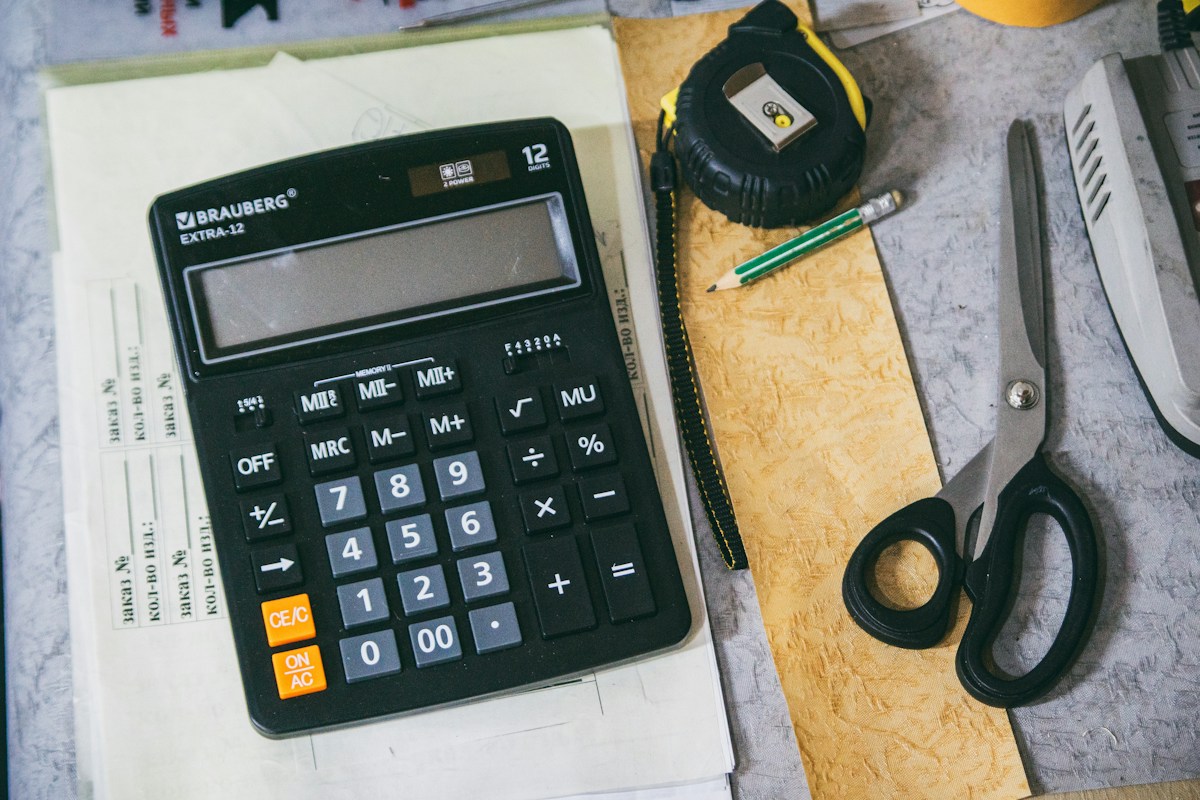 Calculatrice, mètre ruban, crayon et ciseaux sur bureau.