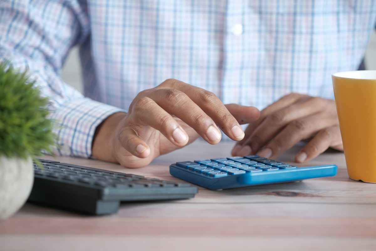 Homme utilisant une calculatrice bleue près d’un ordinateur portable