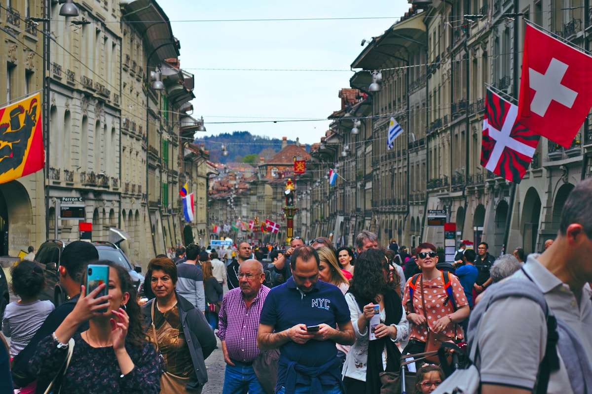 Foule animée dans une rue commerçante de Berne, Suisse, avec drapeaux et bâtiments historiques.