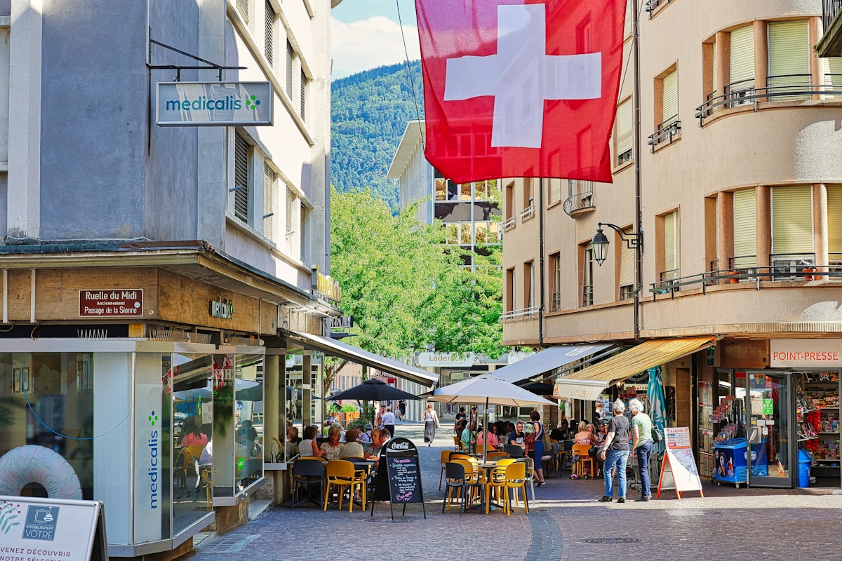 Rue animée avec drapeaux suisses, cafés et commerces.