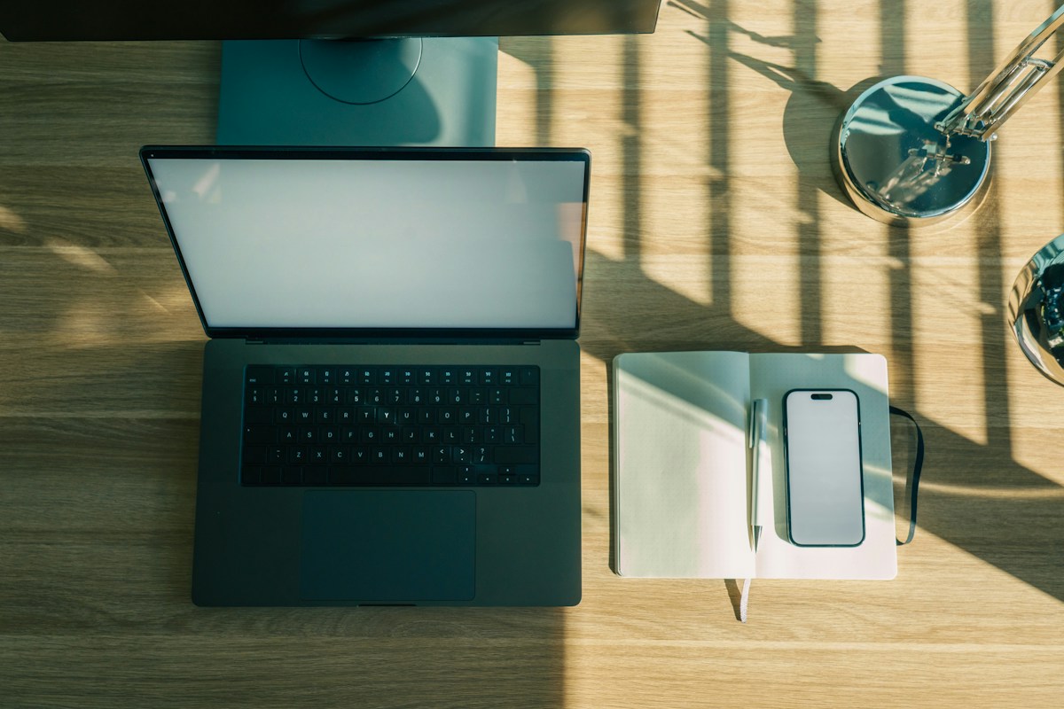 Bureau en bois avec ordinateur portable, carnet, smartphone et lampe.