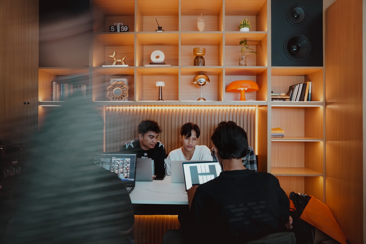 Trois jeunes hommes travaillant ensemble sur des ordinateurs portables dans un espace de travail moderne.