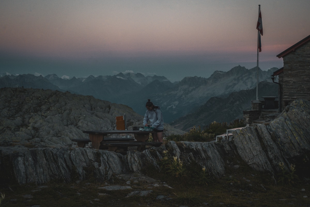Paysage montagneux au crépuscule, cabane de montagne, personne assise à l'extérieur.