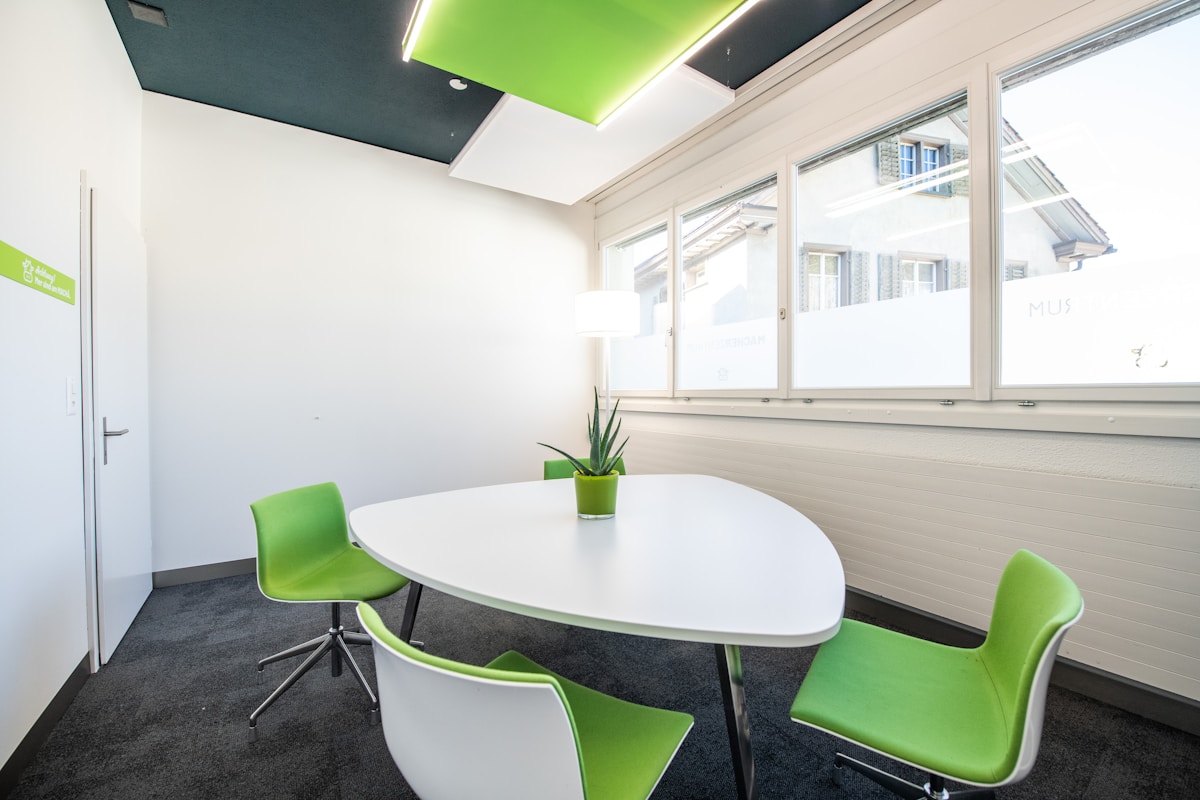 Salle de réunion moderne avec table blanche et chaises vertes.