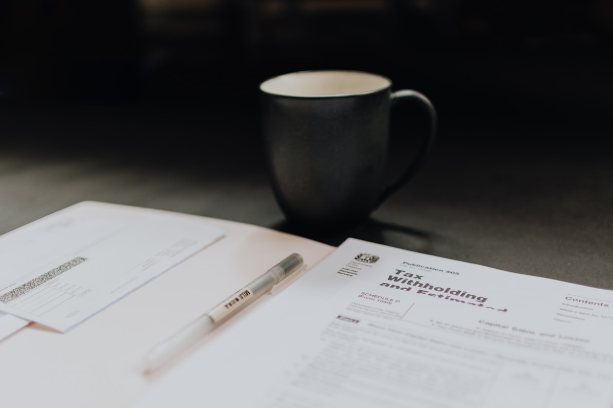 Tasse de café, documents, stylo sur un bureau sombre.