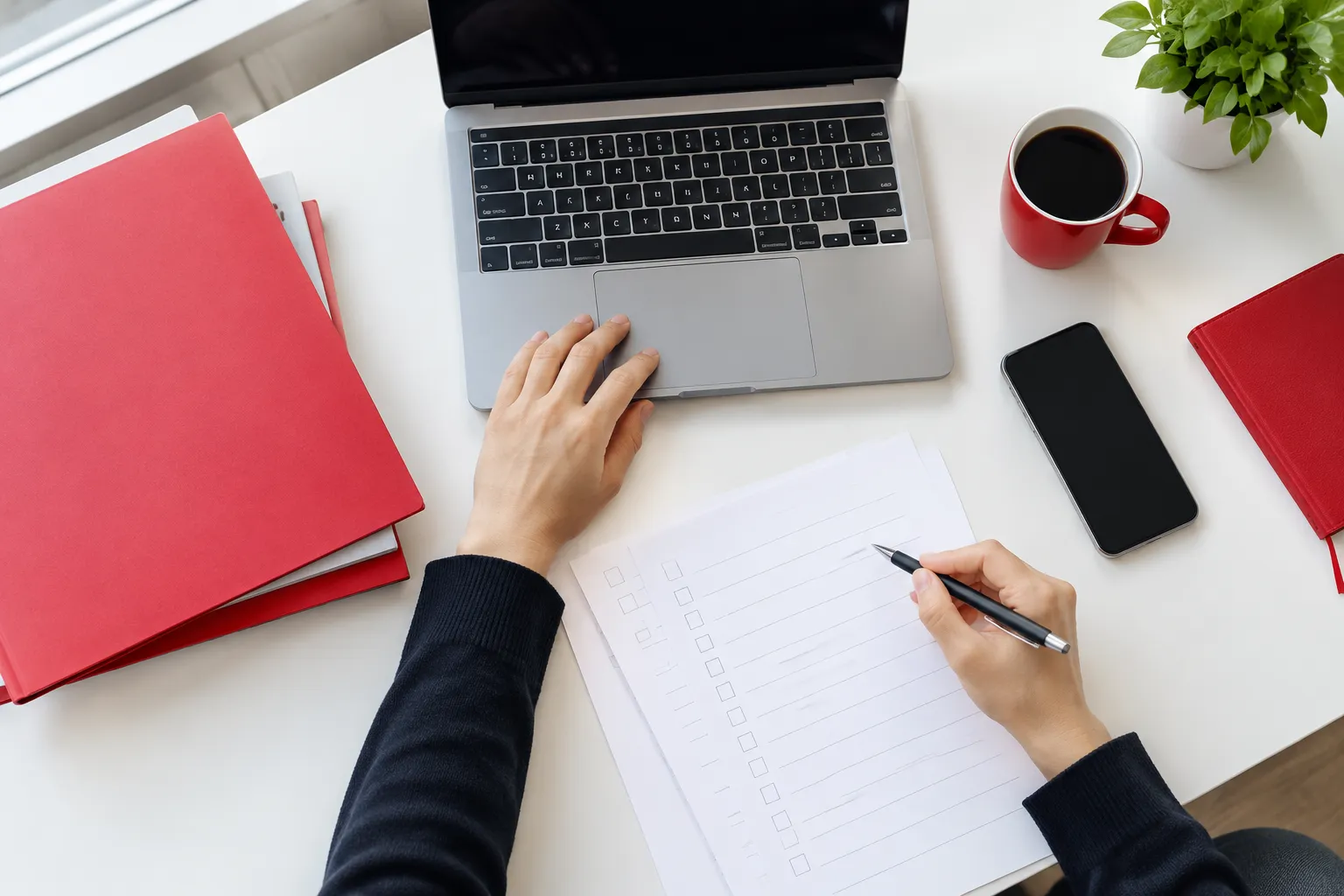 Person working at laptop with checklist, coffee, and notebooks