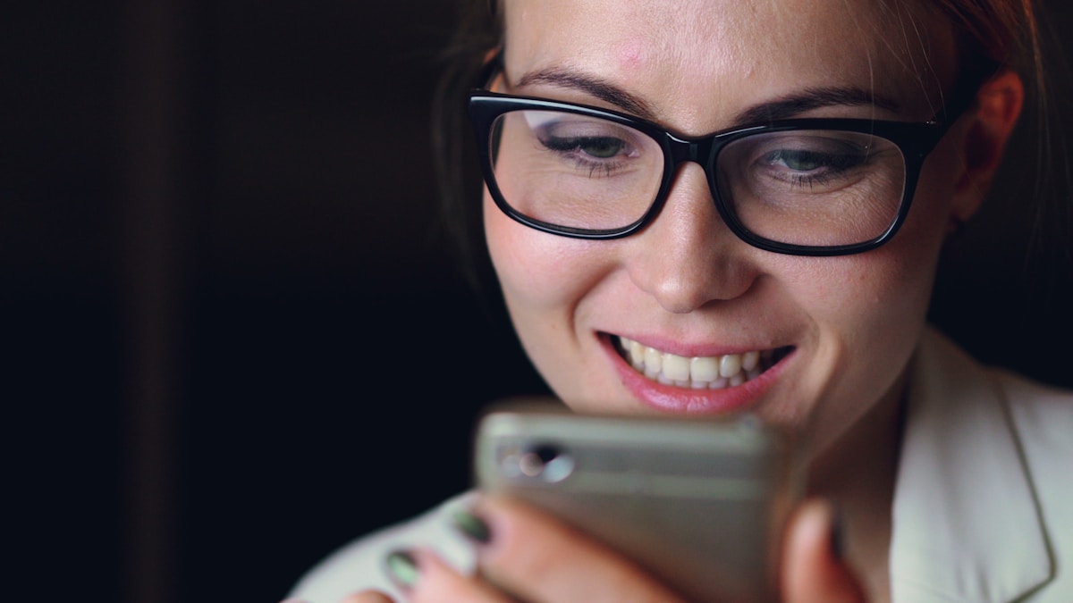 Woman wearing glasses smiles at her smartphone