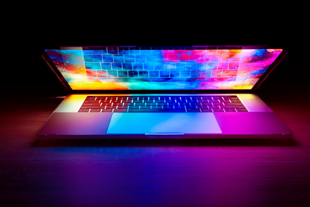 A laptop with a vibrant colorful screen glowing on a dark wooden desk