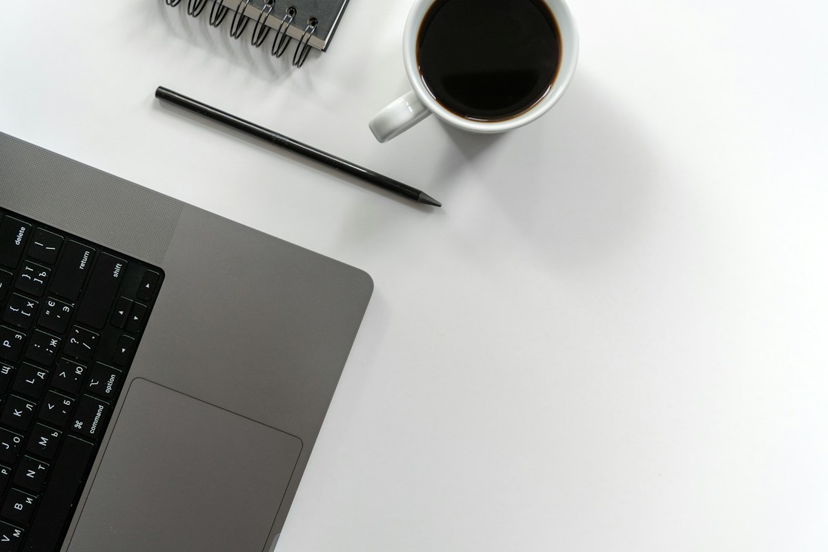 Laptop, coffee, pen, and notebook on a white desk