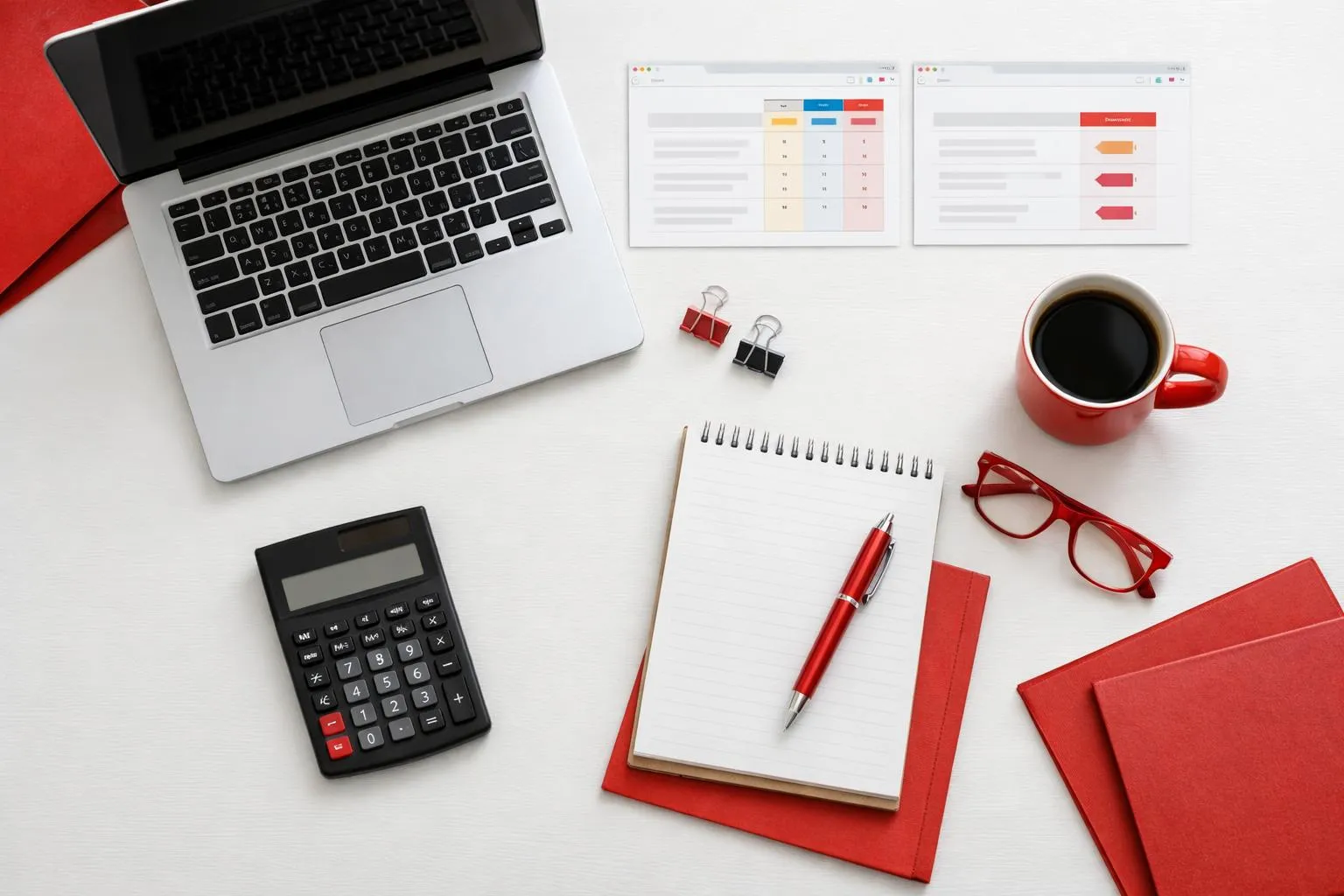 Laptop, calculator, notebook, coffee mug, and office supplies on white desk.