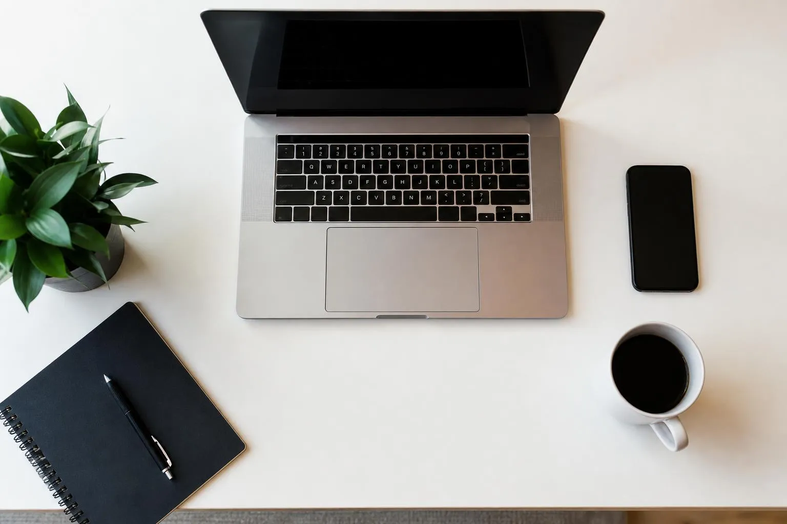 Laptop, smartphone, notebook, and coffee cup on a white desk.