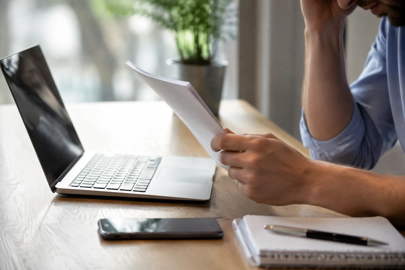 Person working on laptop, documents, and mobile phone on desk.
