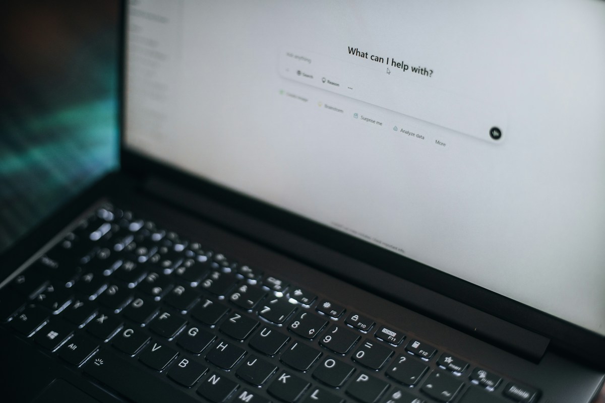A laptop displays "what can i help with?"