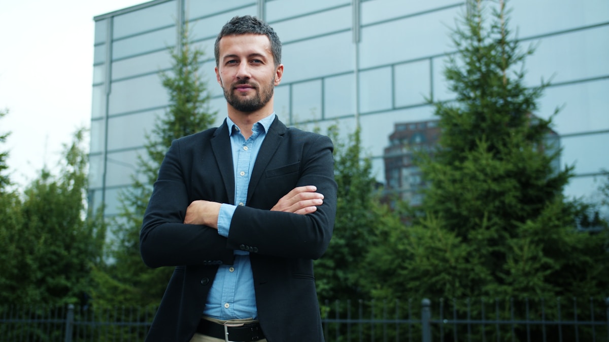 Man in suit standing with arms crossed outdoors.