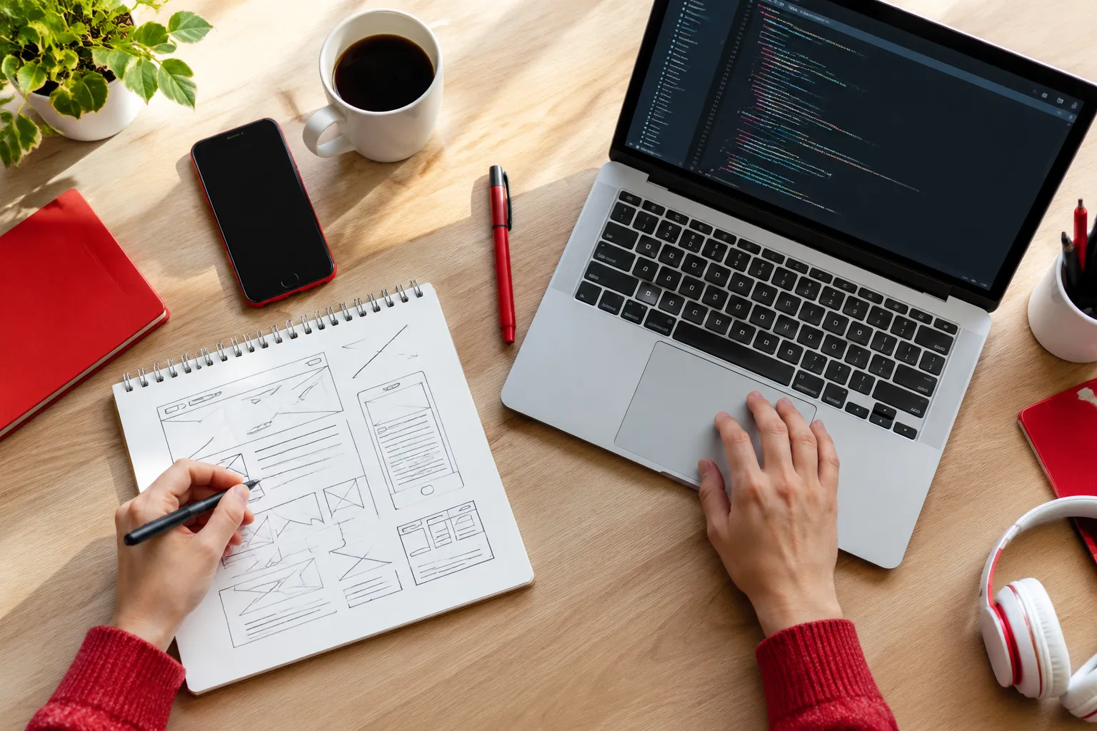 Web designer sketching wireframes beside coding laptop and coffee