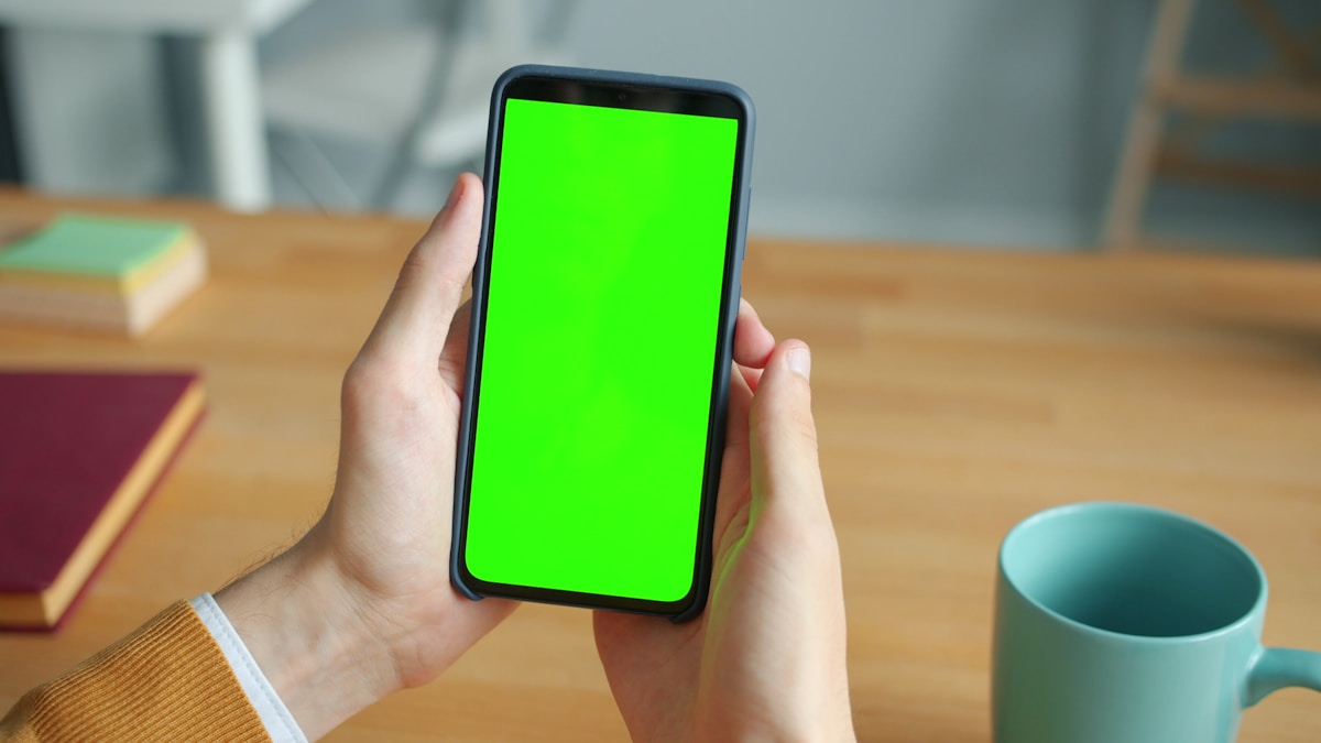 Hands holding a smartphone with a green screen.