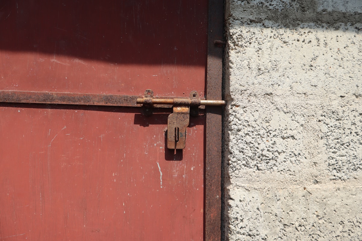 Porte de grange rouge avec verrou rouillé et mur en béton.