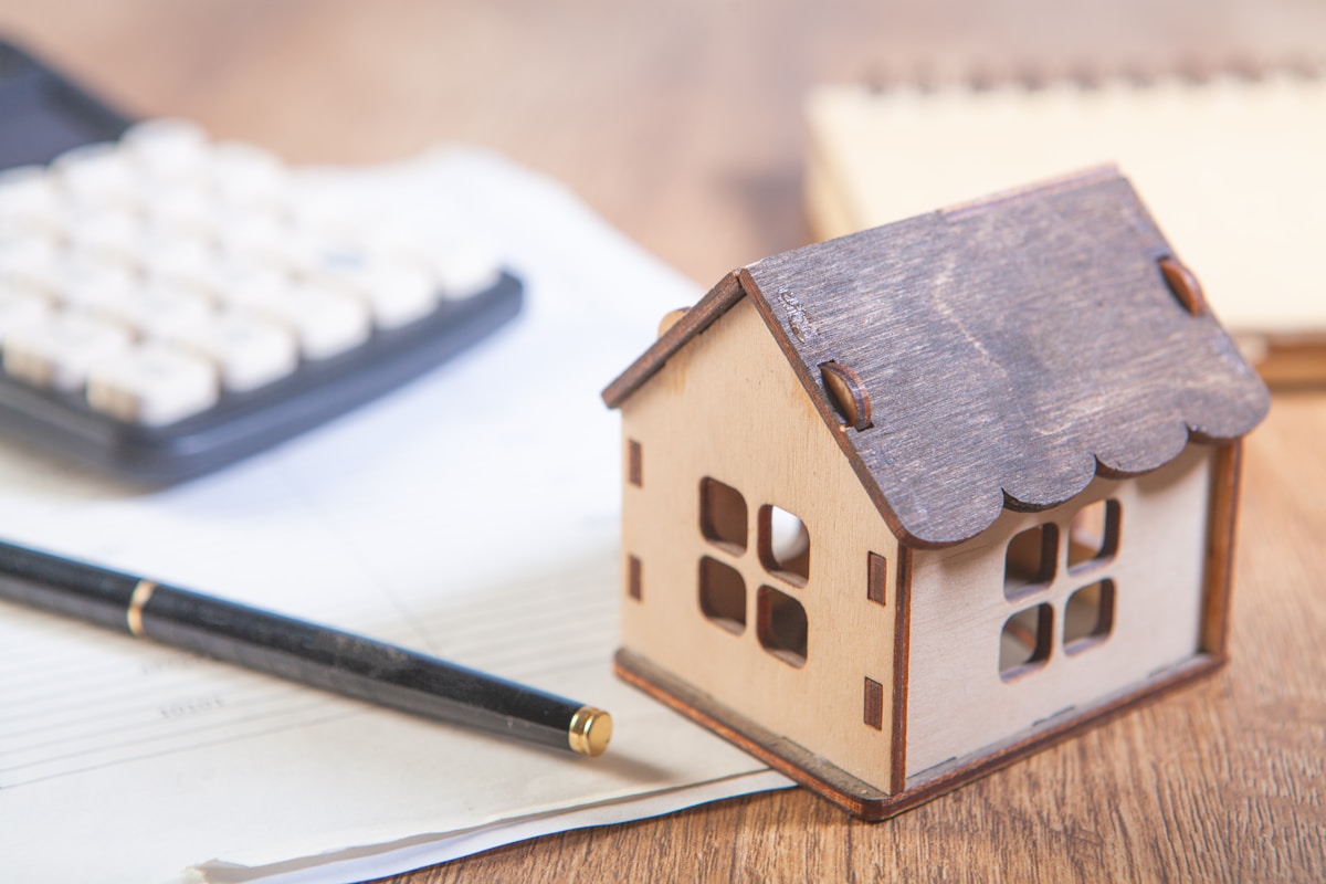 Modèle de maison en bois, calculatrice et documents sur un bureau.