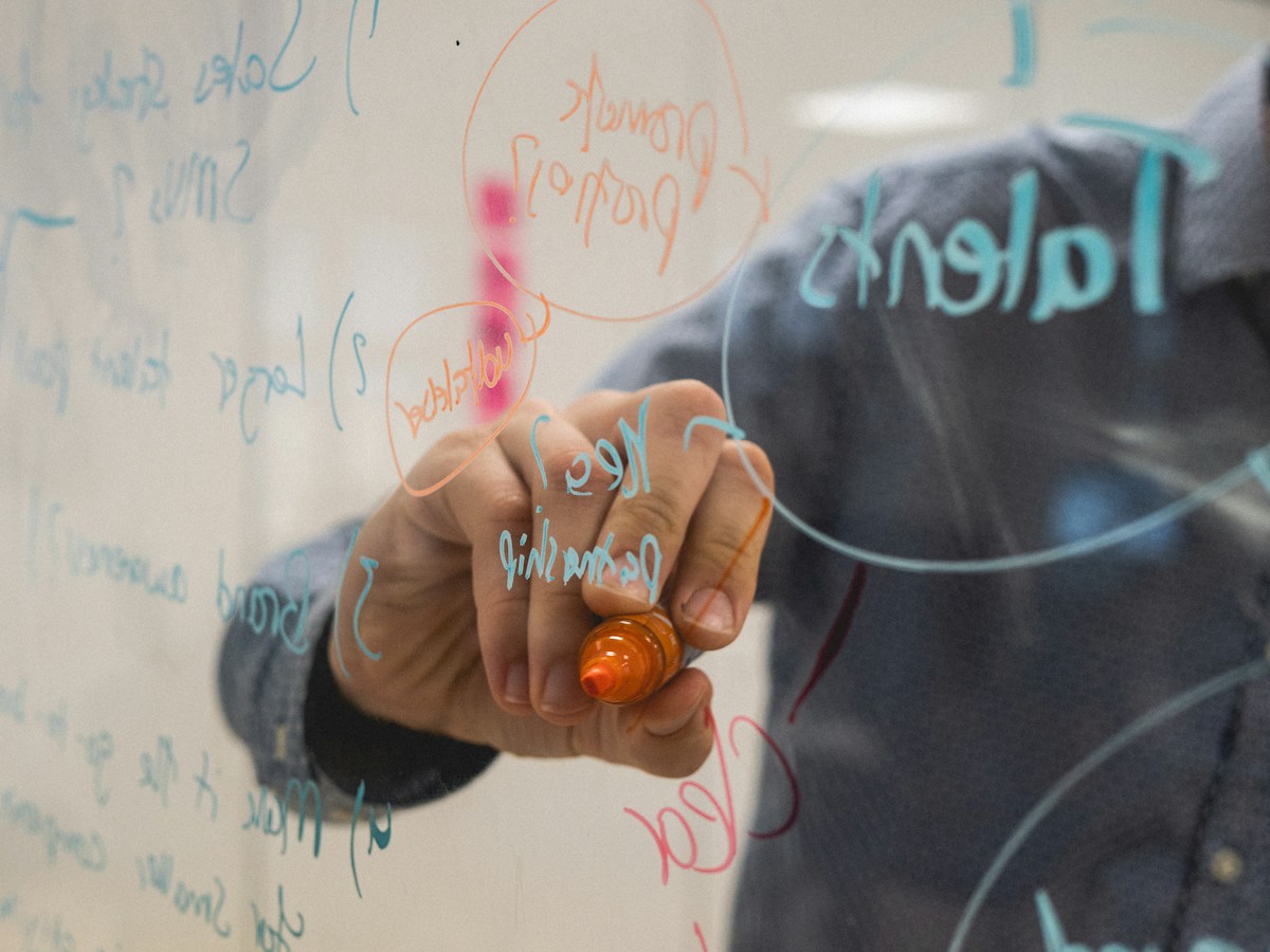Personne écrivant des notes colorées sur une vitre transparente.