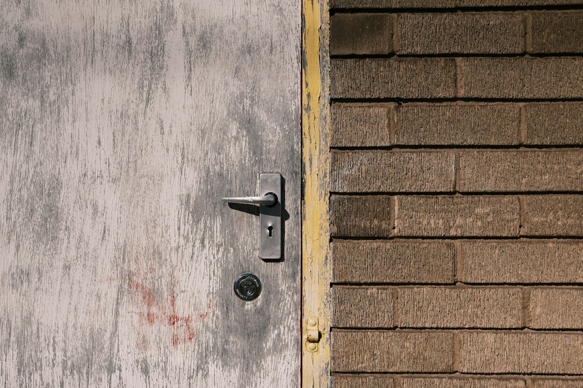 Porte grise usée avec poignée métallique, mur de briques brunes