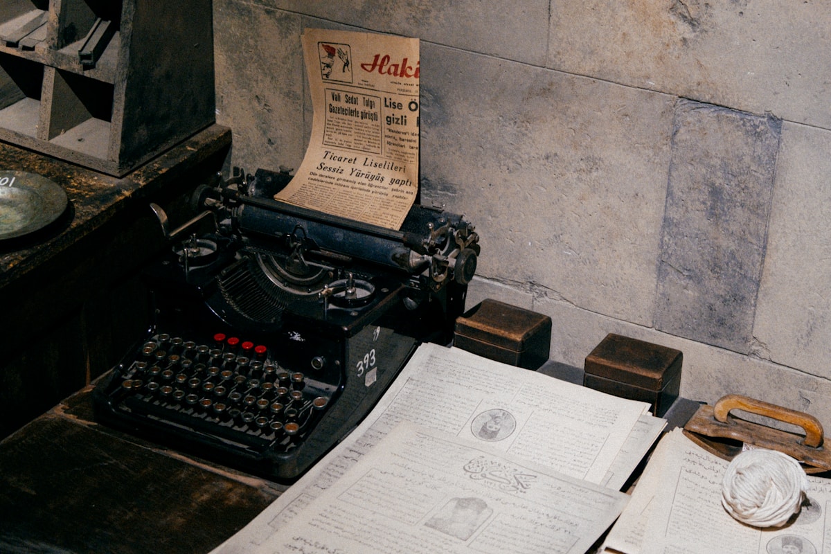 Ancienne machine à écrire, journaux et papiers sur un bureau vintage.