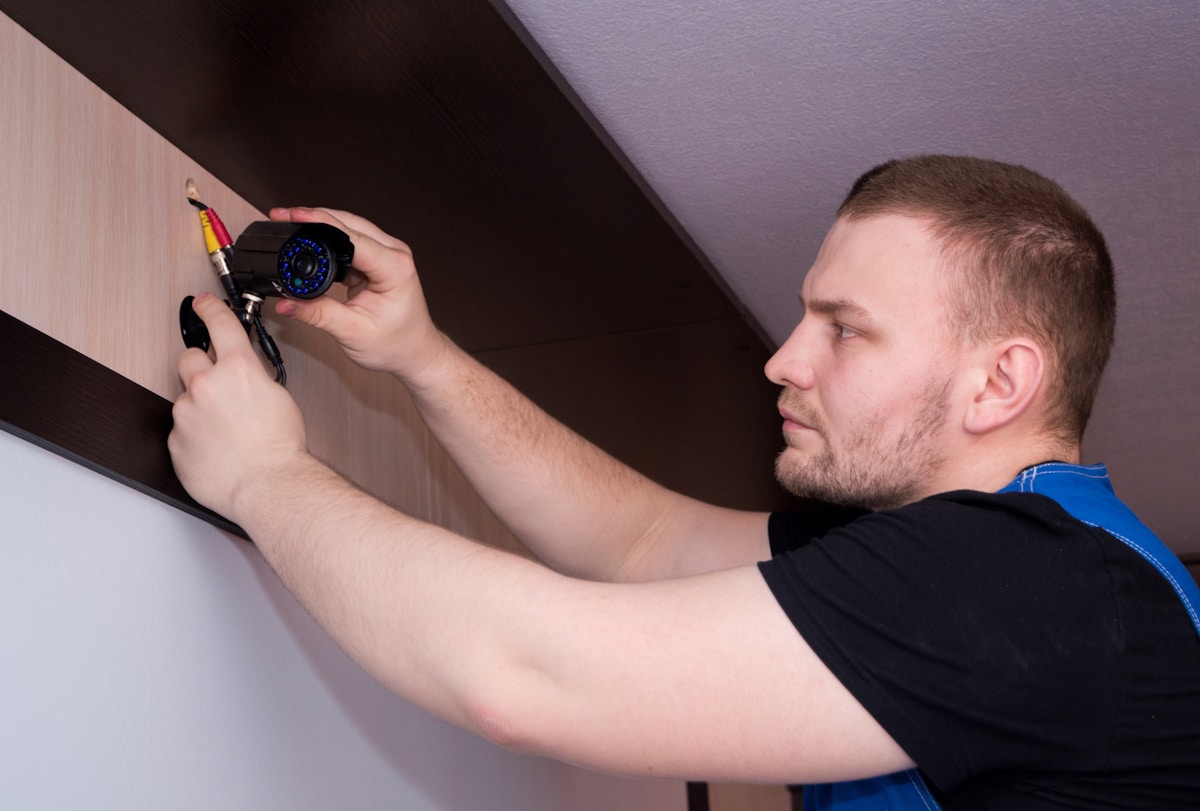 Un homme installant une caméra de sécurité sur un mur.