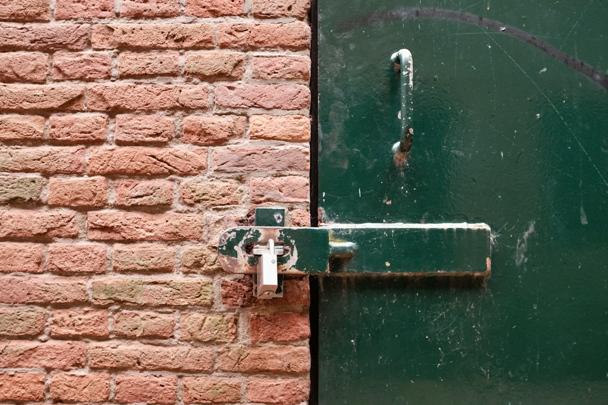 Verrou métallique usé sur porte verte et mur de briques rouges