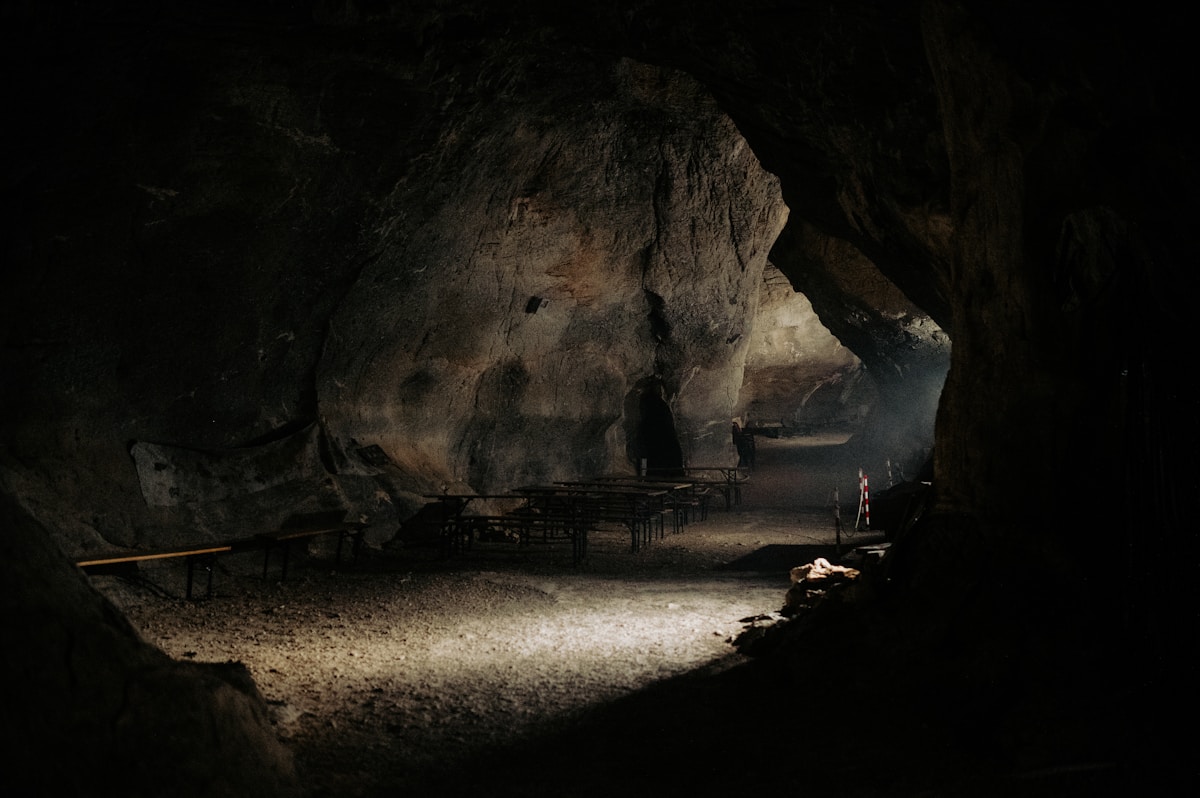 Grotte sombre avec éclairage artificiel, bancs et sol rocheux.