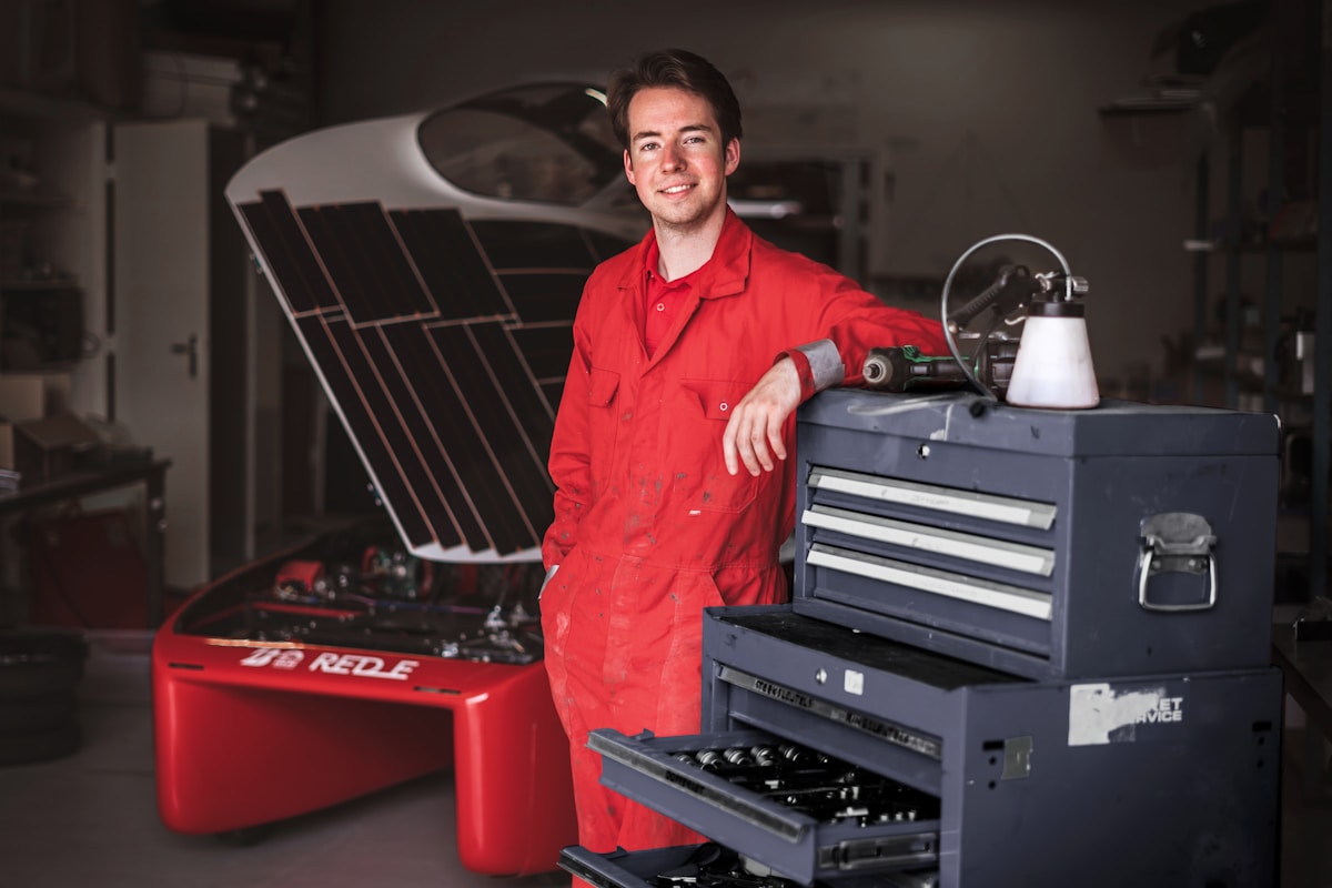 Mécanicien en uniforme rouge souriant dans un atelier automobile.