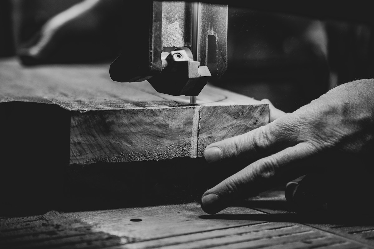 Main d’artisan guidant du bois sous une scie à ruban