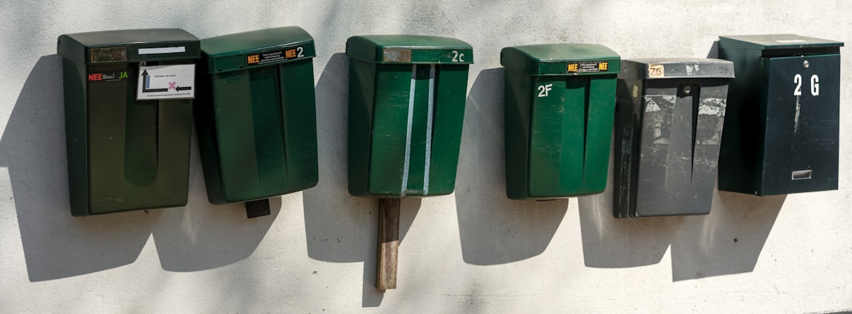 Boîtes aux lettres vertes alignées sur un mur gris.