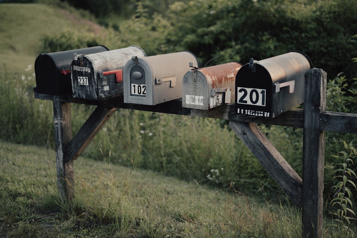 Boîtes aux lettres rustiques alignées sur un poteau dans un paysage champêtre.