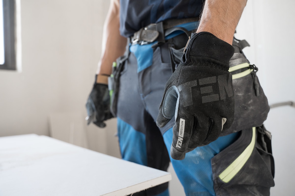 Gants de travail noirs et bleus avec logo, sur un ouvrier en tenue de travail.